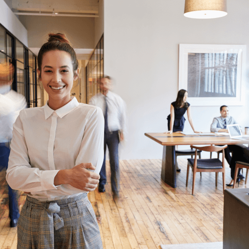 Confident businesswoman in a modern office environment, and colleagues in motion around her.