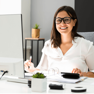 A smiling professional woman in a white blouse sitting at a modern desk with documents